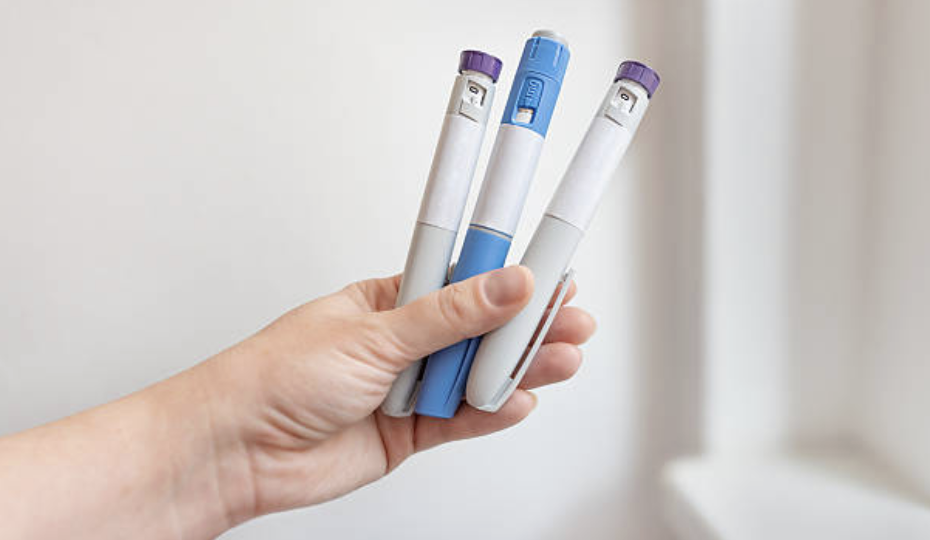 Hand holding three weekly GLP-1 injection pens used for weight loss