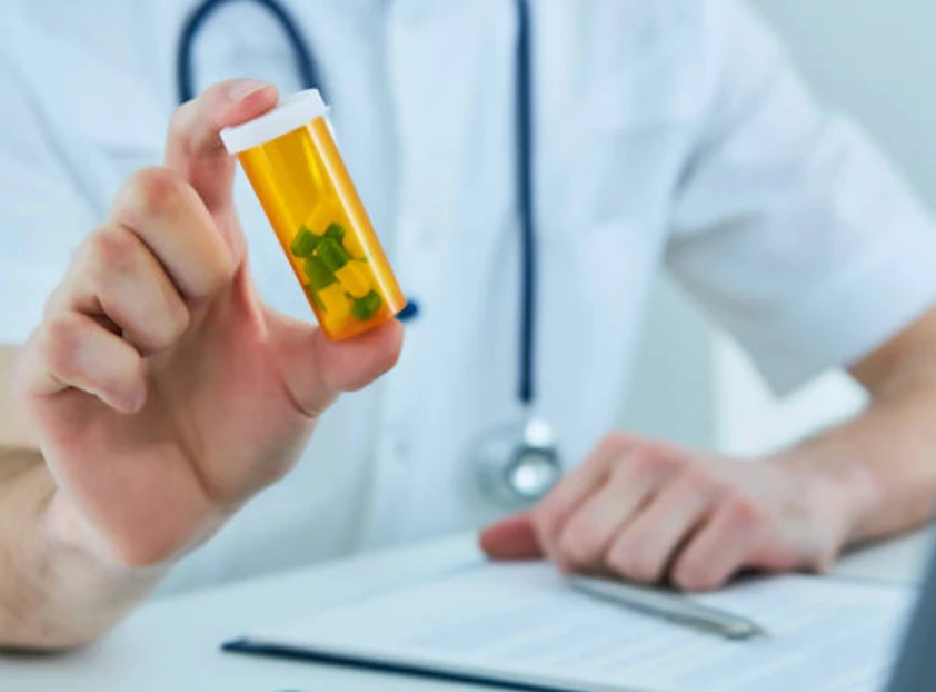Physician holding up a prescription pill bottle at a desk