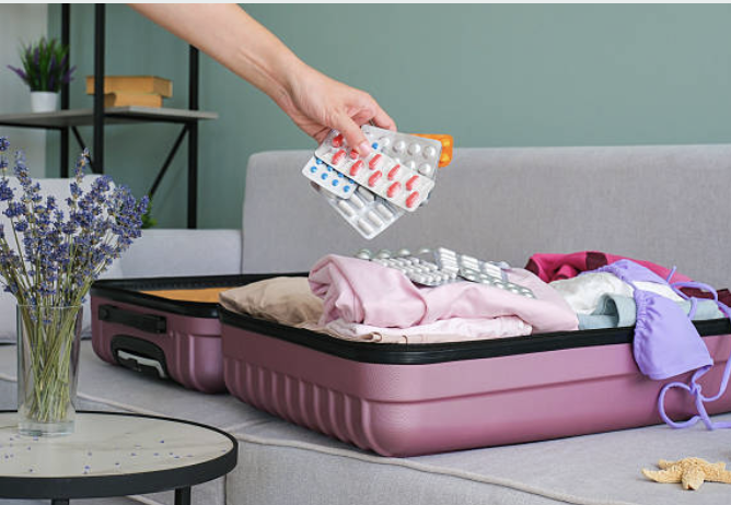 Hand placing blister packs of medication into an open suitcase before a trip